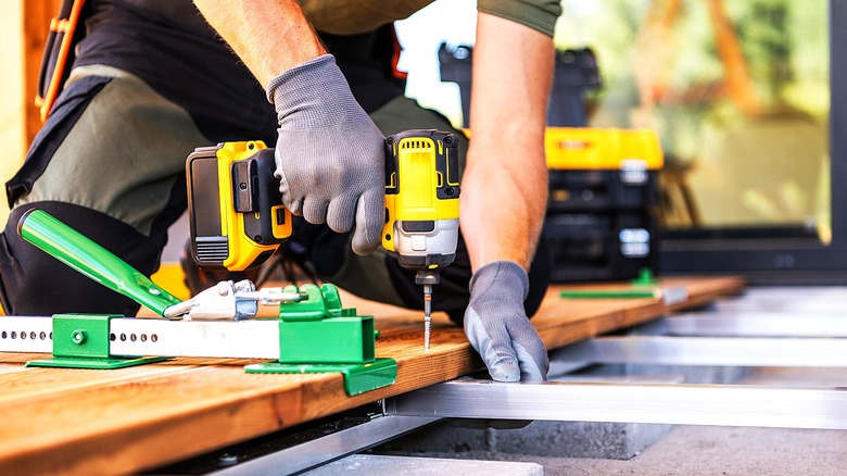 A person installs decking using a yellow power drill
