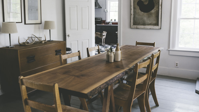 Rustic dining room with a long wood table with natural edges, wooden chairs, and rustic art.