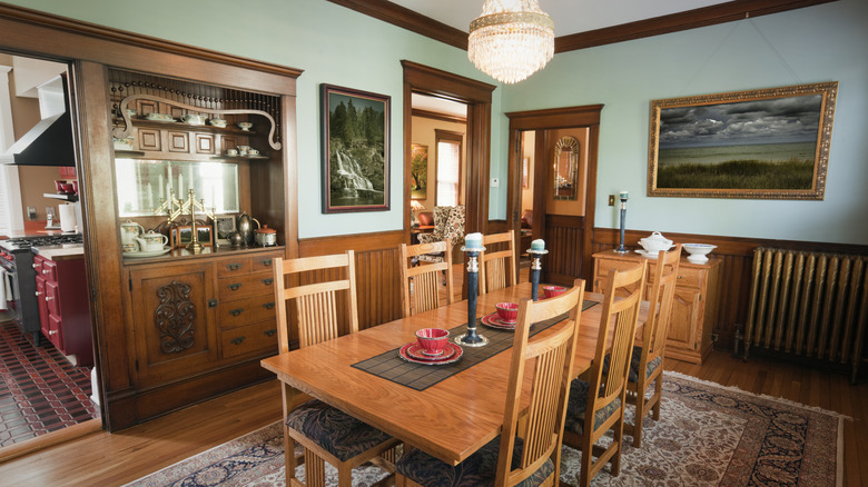 Victorian dining room with wooden table and matching chairs, landscape art, a built-in cabinet, and a chandelier.