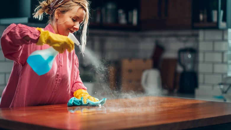 woman spraying countertop with cloth in hand