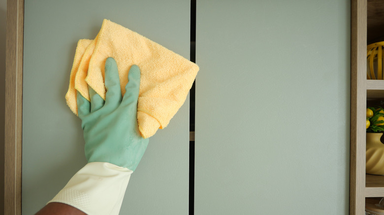 hand wiping down kitchen cabinet with cloth