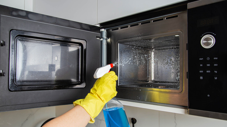 hand spraying cleaner into microwave