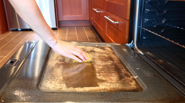 hand wiping the inside of an oven door clean with spong
