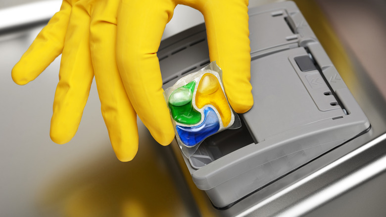 Hand with yellow glove putting dishwasher pod into dishwasher