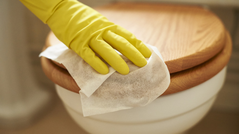 gloved hand using cleansing wipe on toilet lid