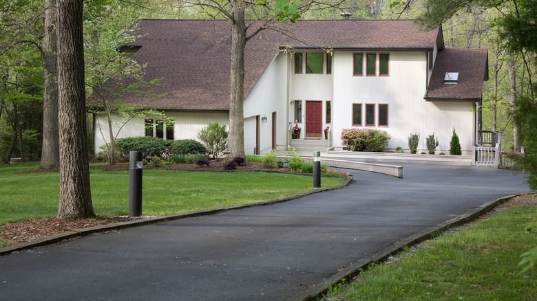 A modern home in the woods with a long asphalt driveway