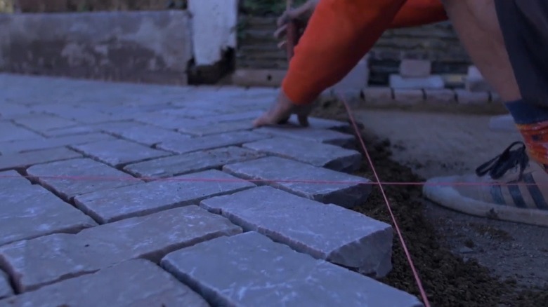 Person installing Indian sandstone pavers on a driveway