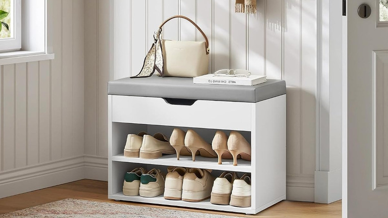 A Vasagle white and gray shoe bench filled with shoes and accessories set in a entryway of a modern home.