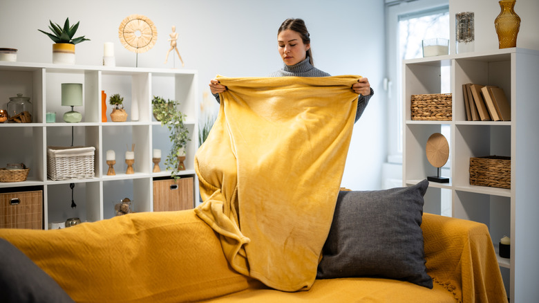 Woman standing in a living room folding a yellow blanket.