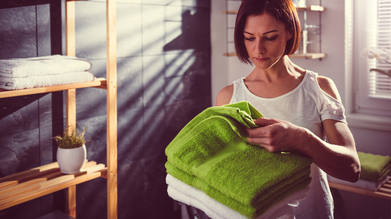 A woman examines the towel on top of the stack of towels she's holding in her arms in a bathroom.