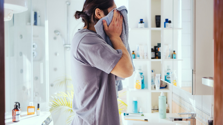 A man in a bathroom surrounded by cluttered shelves