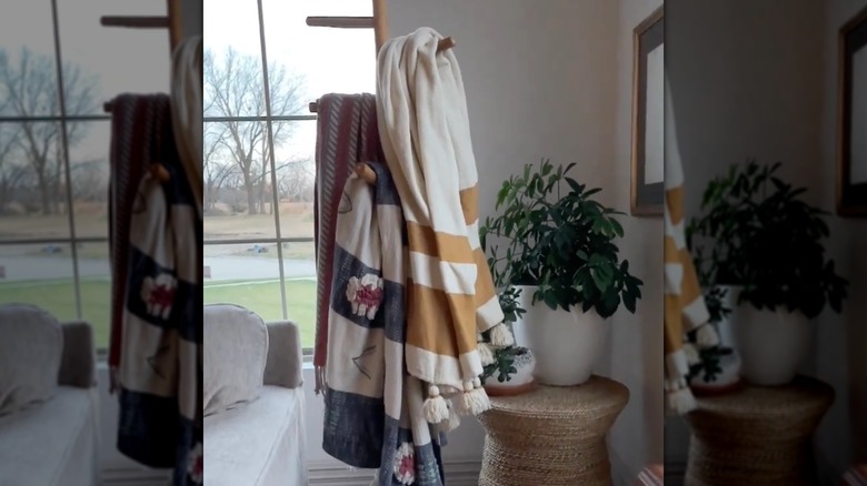 A freestanding coat rack with colorful blankets drapped over it in a stylish living room