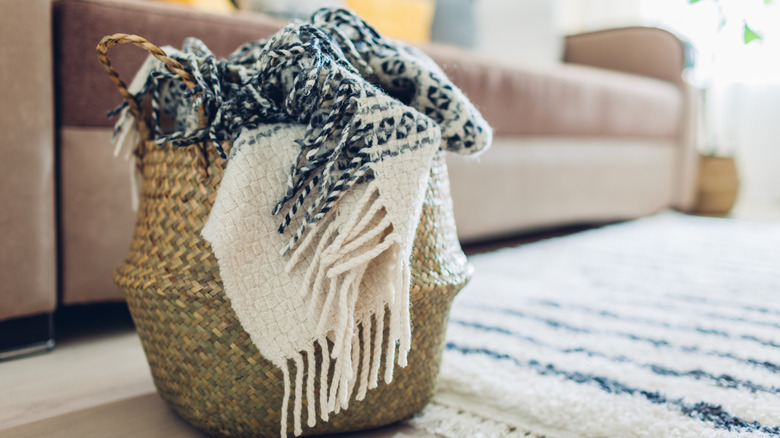 Throw blankets stuffed inside a woven basket on the floor of a living room