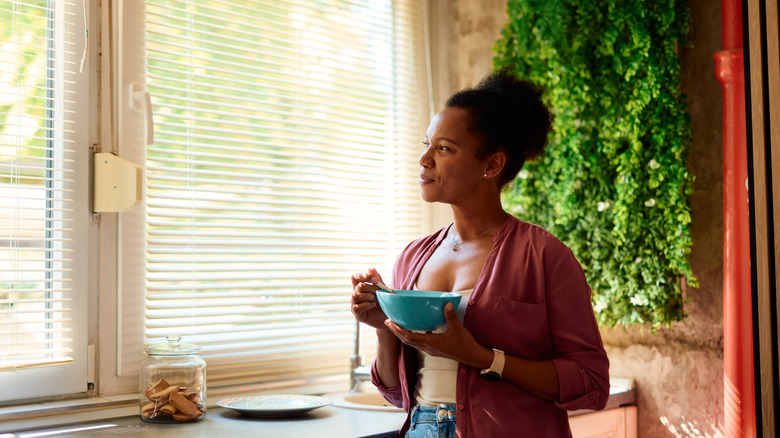 Woman looking out kitchen window with blinds.