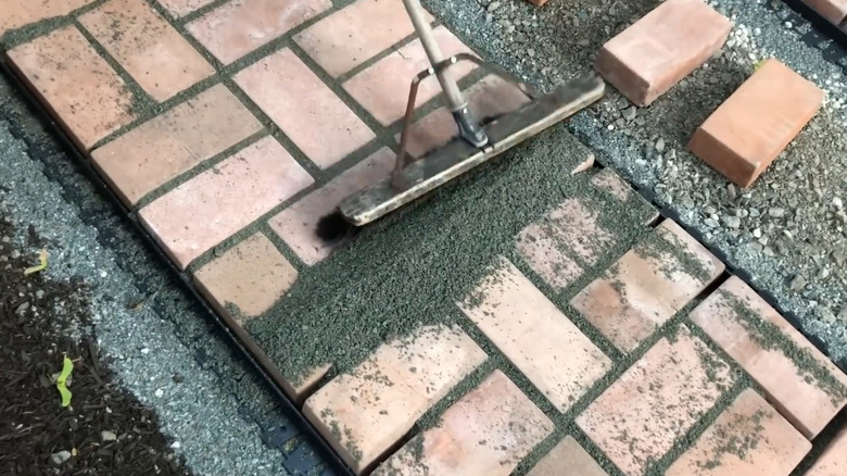 A person filling the spaces between driveway pavers with stone dust