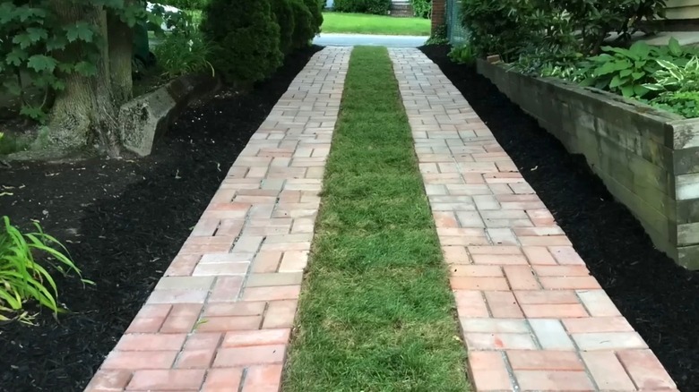 A ribbon brick-paved driveway with green grass in the middle