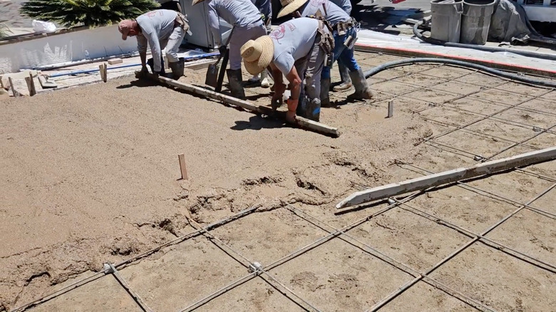 A group of workers laying a beige concrete driveway