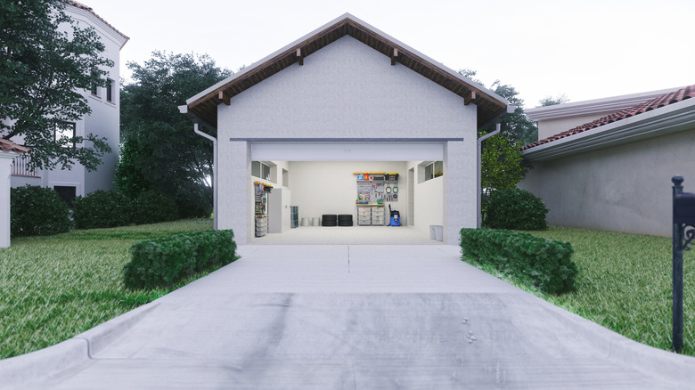 A plain, concrete driveway with grass on each side leading up to a small garage with the door open