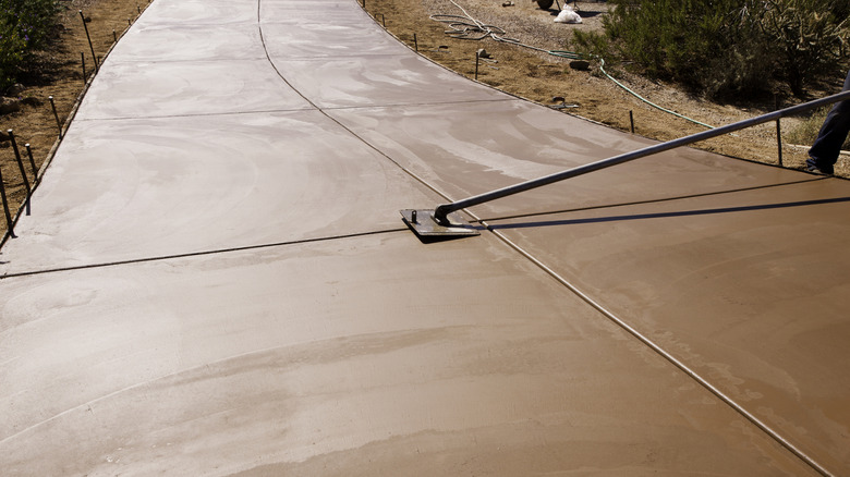 A worker puts the finishing touches on a smooth, red-colored concrete driveway