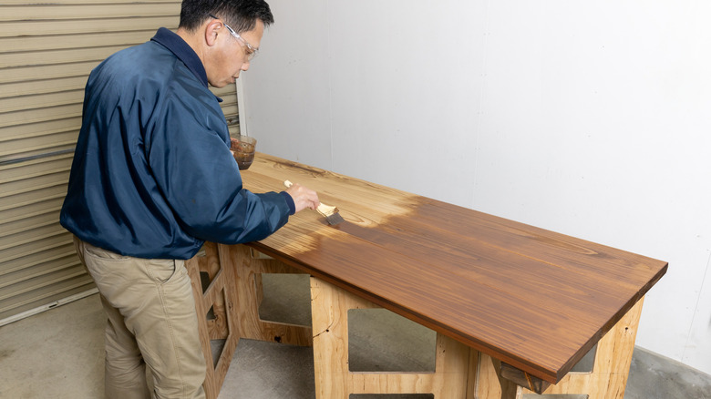 A person paints a wooden board for a DIY project in a garage