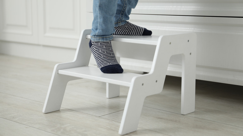 Closeup of someone wearing jeans and socks standing on a bulky wooden step stool in the kitchen