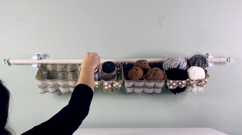 A woman places craft supplies on a DIY hanging storage rack in a craft room.