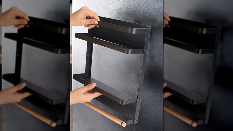 A set of hands holding the magnetic spice wrack against a black fridge