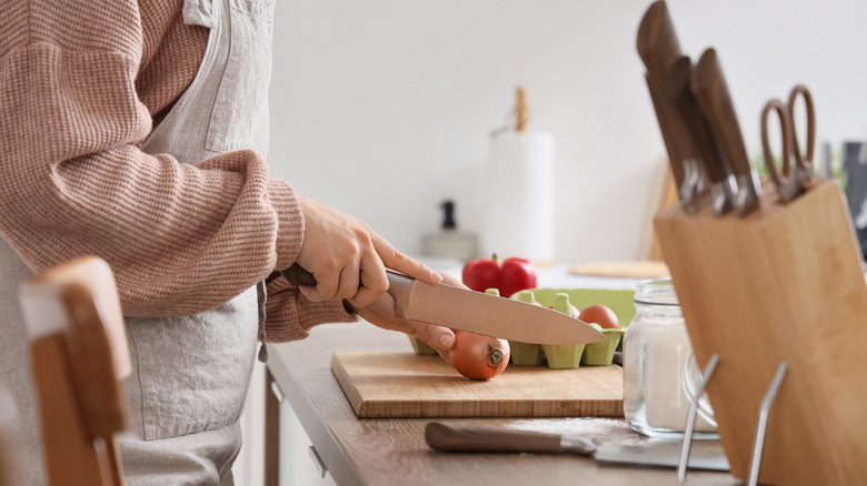 woman cutting produce with a knife next to a knife block