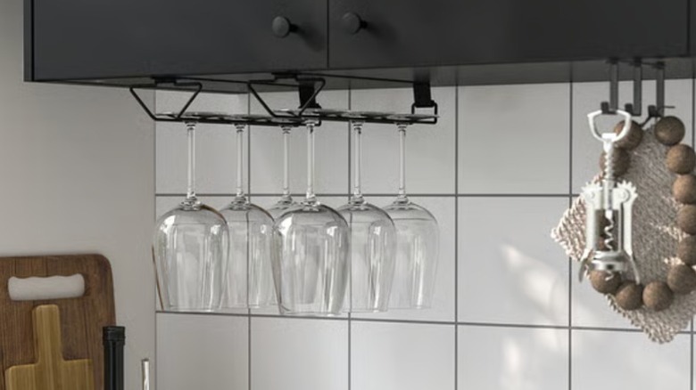 Wine glasses are neatly organized on an under-cabinet hanging rack, freeing up space in the cabinets.