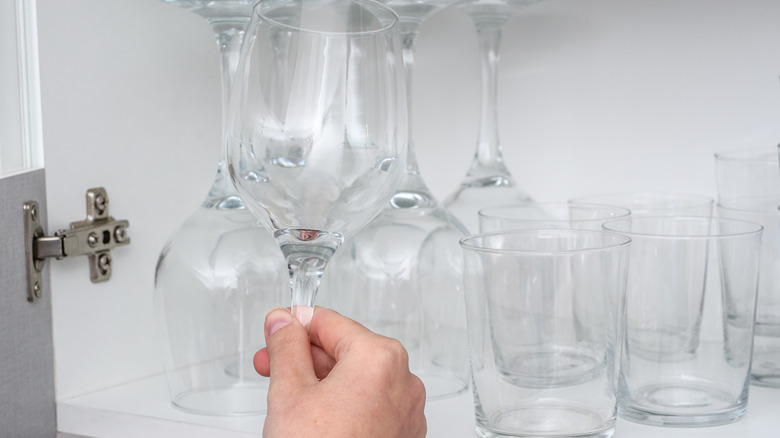 Person pulls a wineglass out of a crowded glassware cabinet.