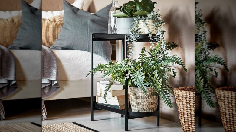 IKEA's OLIVBLAD black steel two-tiered plant stand in a living room holding plants and books