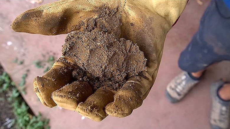 Close-up of a gloved hand holding a ball of rammed earth