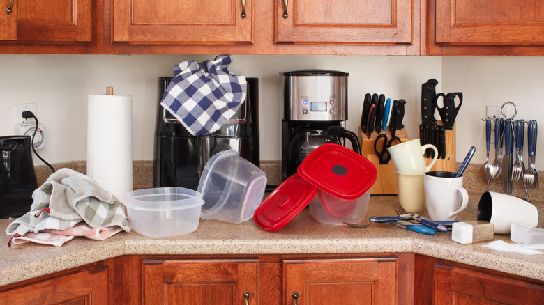 A kitchen counter that is cluttered with mugs, containers, and towels
