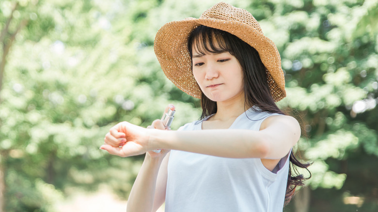 A woman spraying insect repellent onto her arm in a forest-like area