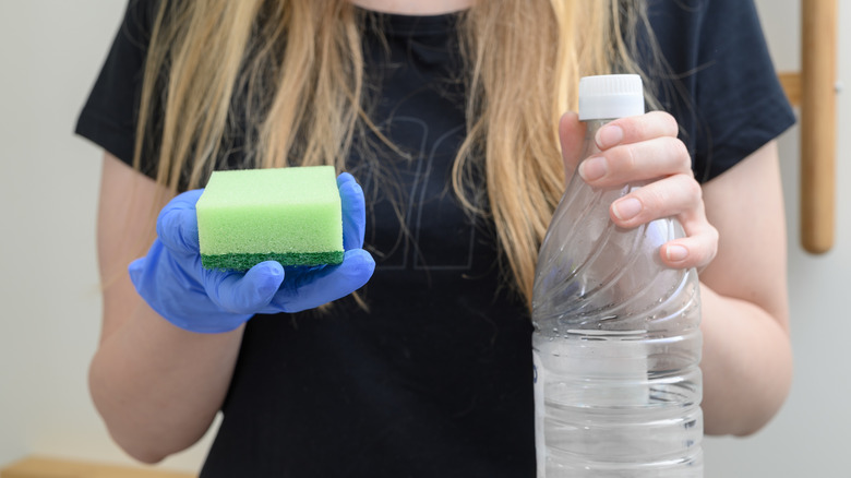 A person holding a sponge and a bottle of vinegar