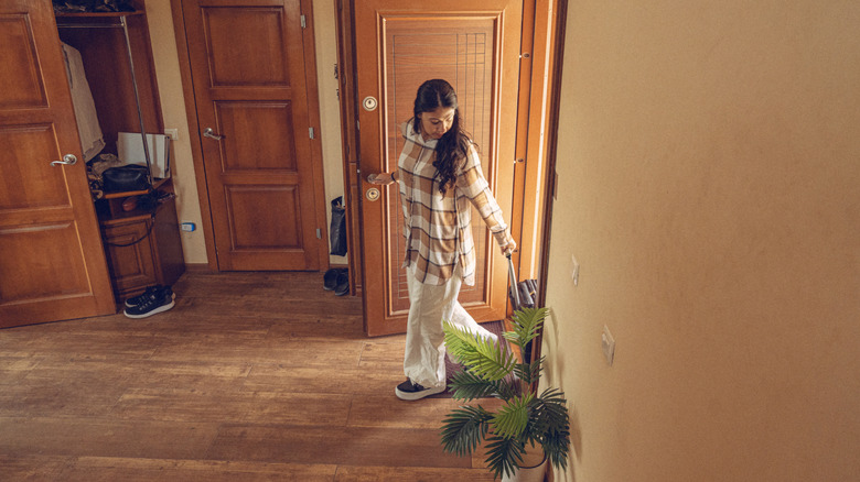 A woman walks into an entryway in her home pulling a small suitcase behind her.