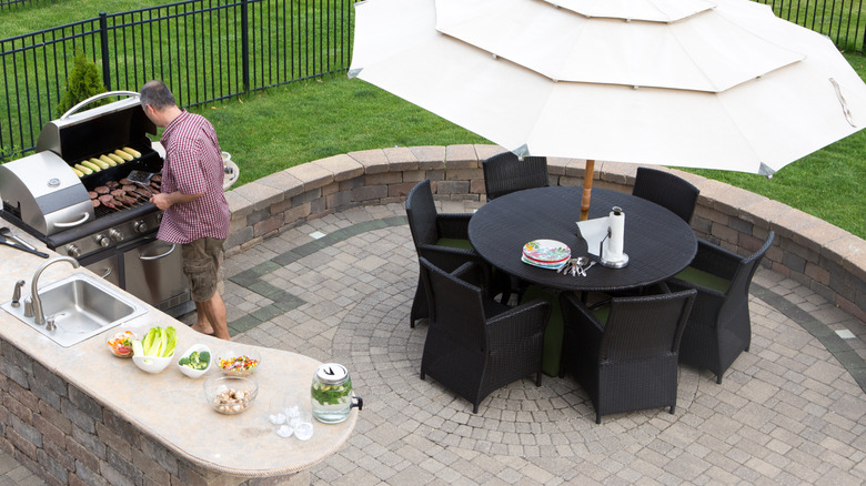 An attractive paver patio with a man cooking on a barbecue