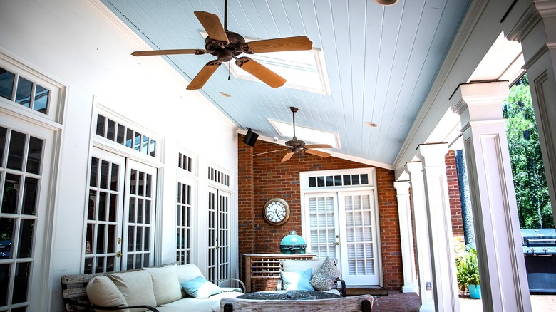 An outdoor living room on a porch cooled by ceiling fans