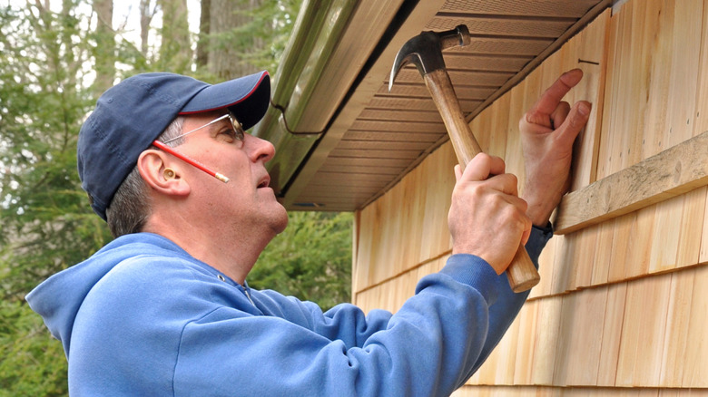 A man installing cedar siding on a house
