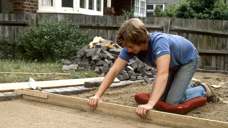 A person prepares a driveway for gravel in a residential front yard.