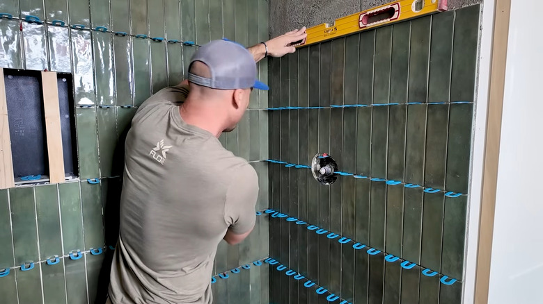 a man installs stacked tiles in a shower stall
