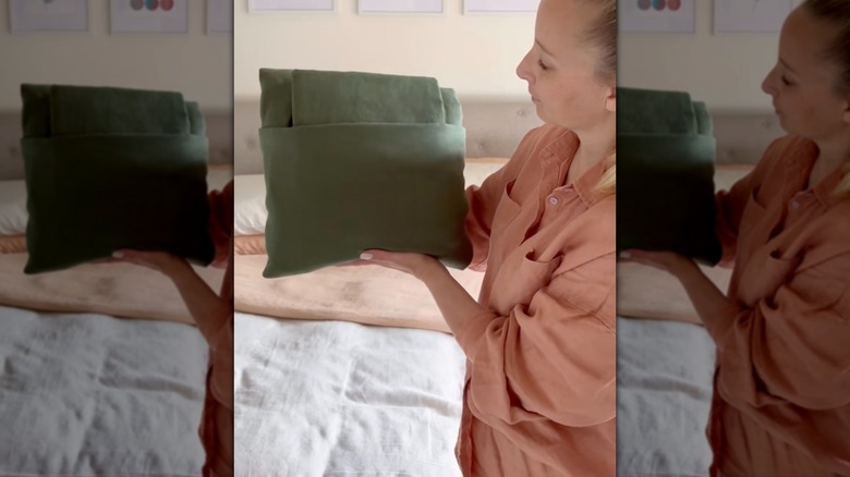 Woman holding a folded bedding bundle including top sheet, fitted sheet, and pillow cases.