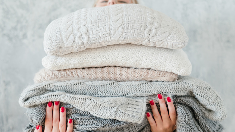 Person holding a stack of blankets and pillows