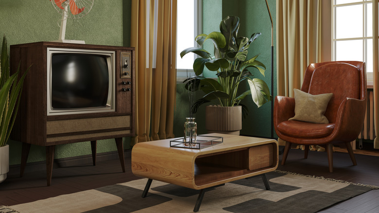 A retro living room with a TV, plant, leather chair, and wooden coffee table