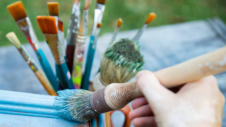 A hand paints a piece of wooden furniture blue.