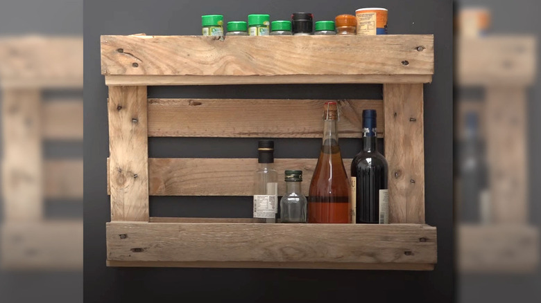 A spice rack made from a wood pallet hangs on a gray wall.