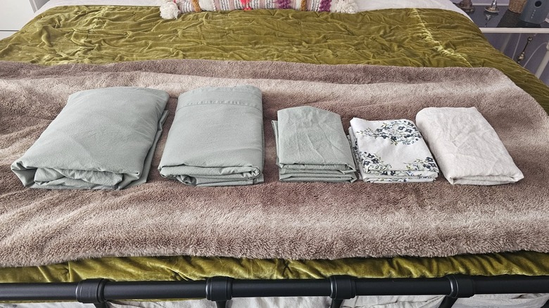 Sheets folded and placed at the foot of a nicely made black wrought iron bed.