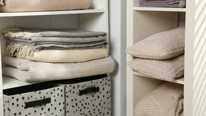 Home textile organization. Folded towels, blankets and pillows on shelving units indoors, closeup
