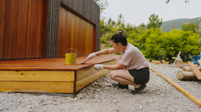 Woman kneeling to paint and seal a wooden deck.