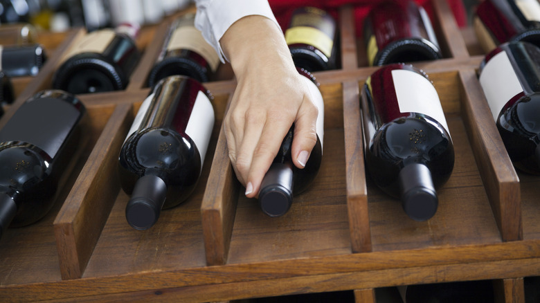 Woman grabbing wine bottle off wooden rack.